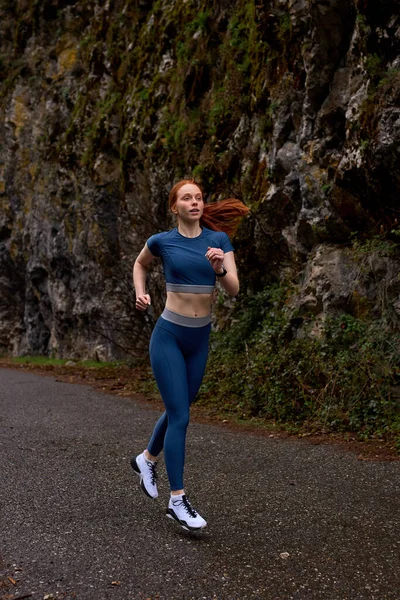 Φοβερός νεαρός καυκάσιος γυναίκα σε μπλε σπορ ρούχα απολαμβάνει τρέξιμο τζόκινγκ στη φύση — Φωτογραφία Αρχείου