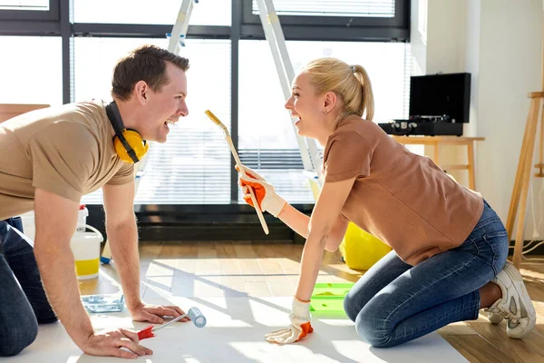 Joyous jovem casal relaxante, pintura em folha de papel em casa nova no chão — Fotografia de Stock