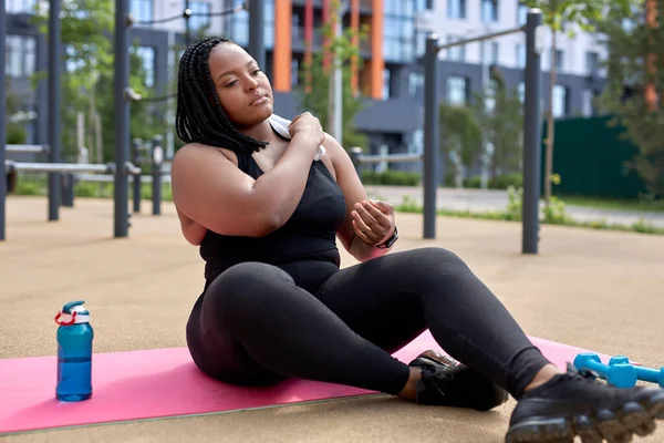 Yorgun, obez bir afro kadın antrenmandan sonra spor minderinde dinleniyor. — Stok fotoğraf