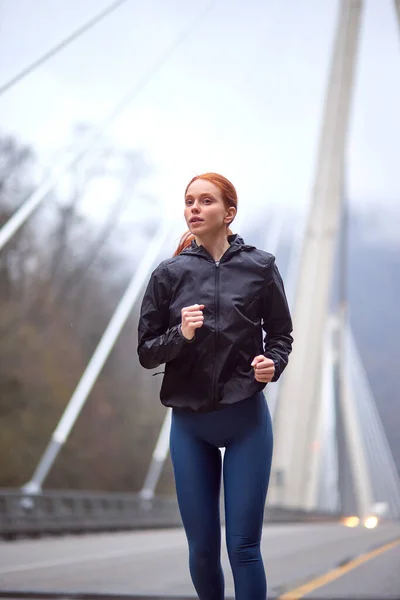 都会のスポーツに自信のある若い女性が寒い春の朝に街をジョギングし — ストック写真