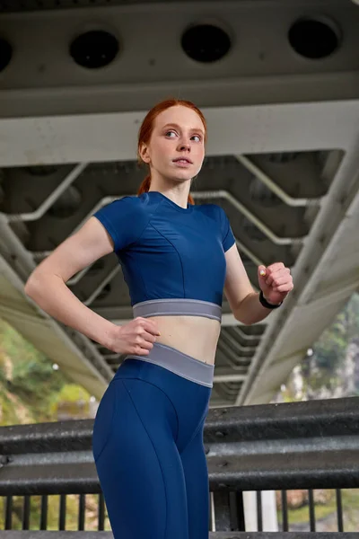 Mooie zelfverzekerde sportvrouw in stijlvolle sportkleding joggen op brug — Stockfoto