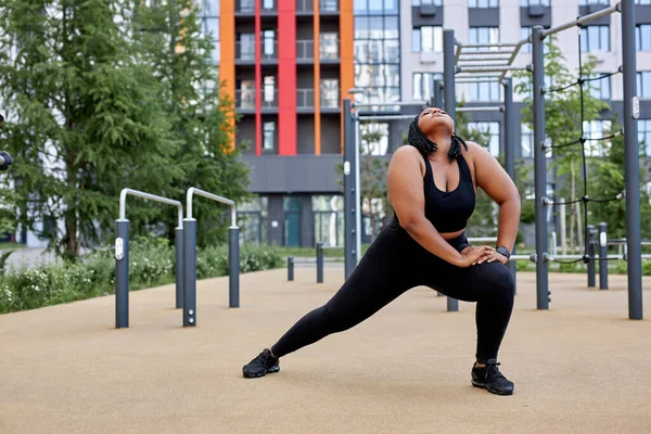 Obez şişman Afrikalı kadın antrenmandan önce spor alanında esneme egzersizleri yapıyor. — Stok fotoğraf