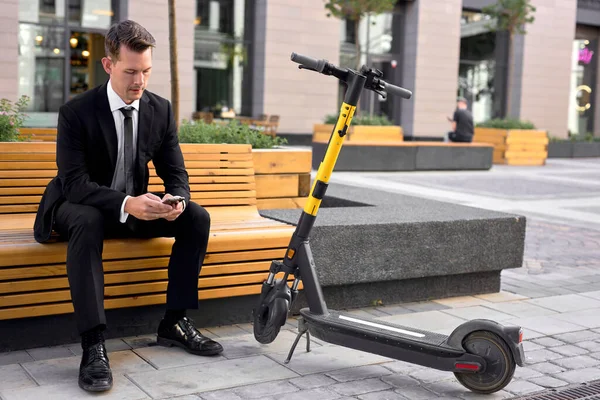 Zelfverzekerde man zit op bank in de buurt trendy stadsvervoer moderne elektrische scooter — Stockfoto