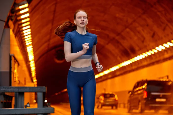 Atleet vrouw loper in blauwe top en leggins vol vertrouwen lopen langs de weg — Stockfoto