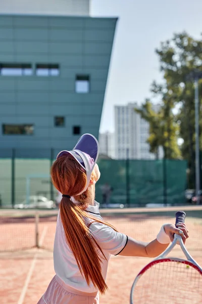 Zadní pohled na násilnou fit žena hrát tenis na venkovním kurtu, trefit míč, trénink — Stock fotografie