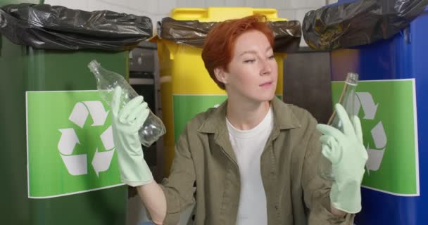 Jonge roodharige dame zit na te denken over het recyclen van afval, het vasthouden van plastic en glazen flessen — Stockvideo