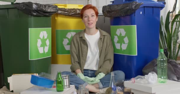 Concepto de Sostenibilidad. Mujer milenaria optimista sentada junto a contenedores con diferentes desechos — Vídeo de stock