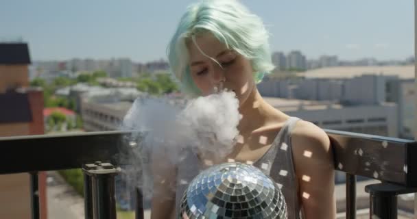 Женщина с короткими зелеными волосами курит электронный пар на балконе — стоковое видео
