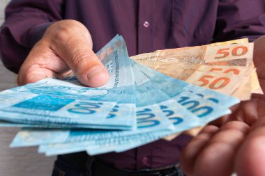 Orta yaşlı bir adam Brezilya para birimi banknotları teklif ediyor. Finansal, kar, kredi, maliyet, satın alma, zengin konsept.