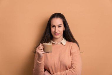 Beyaz bir kadın latte içiyor, stüdyo çekimlerinde bej süveter giyiyor. Portre, gerçek insanlar konsepti..