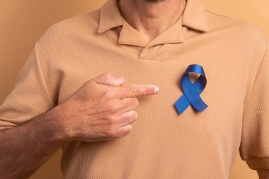Bej arka planda mavi kurdele gösteren Brezilyalı adamın elleri. Prostat kanseri, farkındalık kavramı.