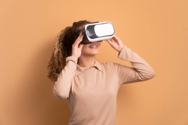 Neşeli genç kız VR kulaklık kullanıyor ve bej arka planda el kol hareketi yapıyor. sanal gerçeklik, teknoloji simülasyon kavramı.