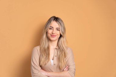 Neşeli beyaz kadın gülümsüyor ve bej renkli stüdyo arka planında kameraya bakıyor. Portre, gerçek insanlar konsepti..