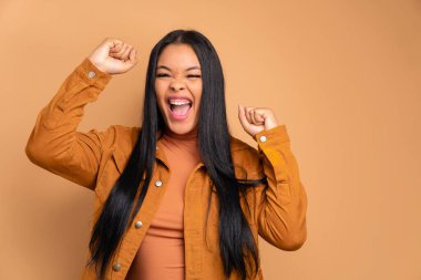 Heyecanlı Afrikalı Brezilyalı kadın kollarını kaldırıp bej rengi stüdyo geçmişiyle kutlama yapıyor. Kutlama, pozitif, başarı konsepti.