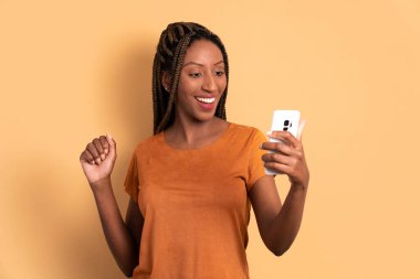 Neşeli Brezilyalı kadın bej arka planda cep telefonu ekranına bakıyor. uygulama, sosyal medya, bağlantı kavramı.