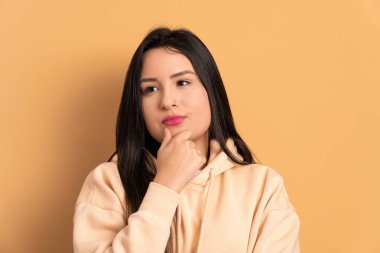 Ciddi genç esmer kadın bej arka planda düşünüyor ve yan bakıyor. Portre, gerçek insanlar konsepti..