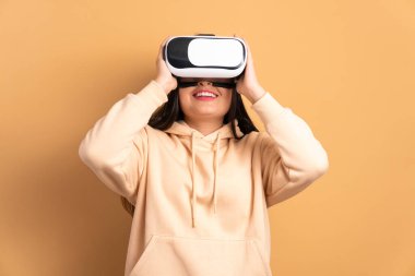 eğlenceli genç esmer kadın VR kulaklık takıyor ve bej renkli jestler yapıyor. sanal gerçeklik, teknoloji simülasyon kavramı.