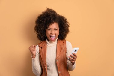 Afro-Amerikalı eğlenceli bir kadın cep telefonundan bej renkli video ve fotoğraf izliyor. Kutlama, pozitif, başarı konsepti.