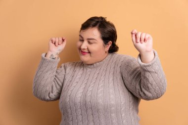 Eğlence artı boyut kadın kollarını kaldırıyor ve tüm bej renkleriyle kutluyor. Kutlama, pozitif, başarı konsepti.