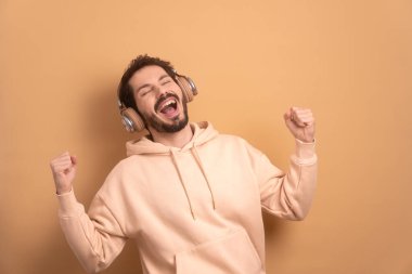 Heyecanlı sakallı adam bej arka planda kulaklıklarla dans ediyor. eğlence, eğlence, müzik, dans konsepti.
