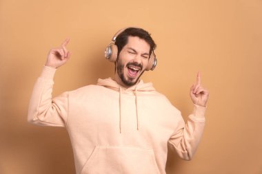 Heyecanlı sakallı adam bej renkli kulaklıklarla dans ediyor. eğlence, eğlence, müzik, dans konsepti.