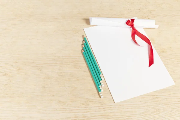 Bir kırmızı kurdele ve ahşap surfac üzerinde kalem kağıt kaydırma — Stok fotoğraf