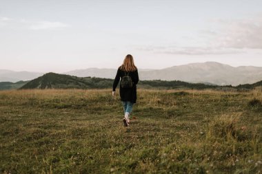 Sırt çantalı bir kadın doğada yürüyor, yeni yerler keşfediyor.