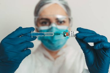 Yüz maskeli kadın doktor elinde kovid 19 aşı tutuyor. 