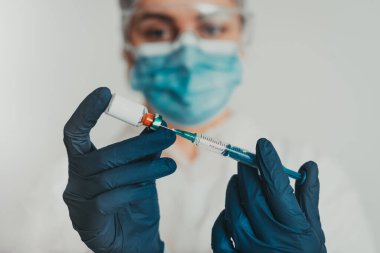 Yüz maskeli kadın doktor elinde kovid 19 aşı tutuyor. 