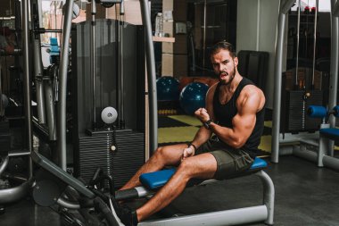 Yakışıklı kaslı adam spor salonunda pazılara ağırlık çalışıyor.