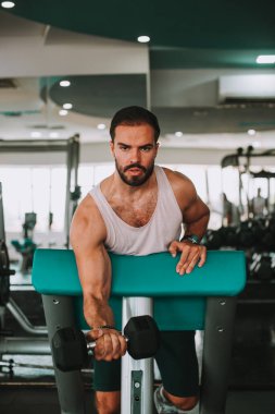 Genç adam spor salonunda dambılla çalışıyor.
