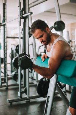 Genç adam spor salonunda dambıllarla çalışıyor.