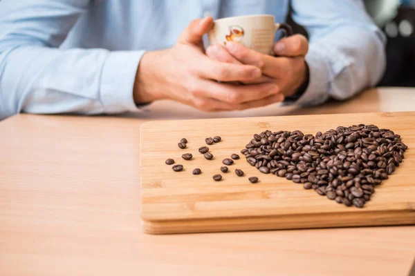 man holding coffee cups in hands and coffee beans on wooden board, closeup