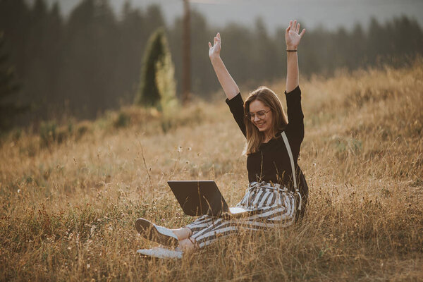 happy woman freelancer with glasses working on laptop, remote location in nature