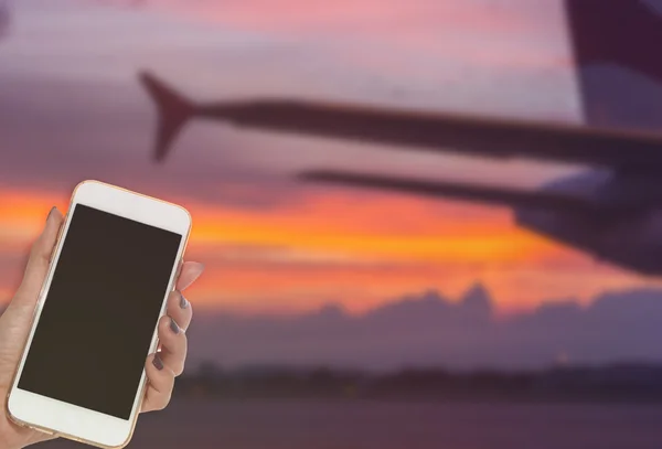 Mujer mano mantenga el teléfono inteligente en el ala de la aeronave, fondo del amanecer —  Fotos de Stock