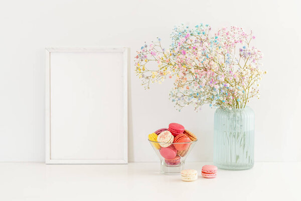 Сладкие красочные макароны и цветочная гипсофила с белой рамкой на столе. 