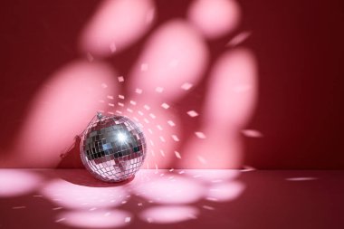 Shiny disco ball, also known as mirror ball, on a pink surface with scattered light reflections.