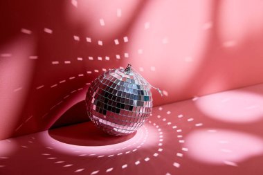 Shiny disco ball, also known as mirror ball, on a pink surface with scattered light reflections.