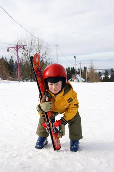 Menino de capacete vermelho levantar esqui — Fotografia de Stock