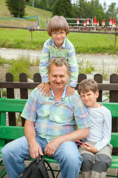 Abuelo de dos nietos sentados en el banco —  Fotos de Stock