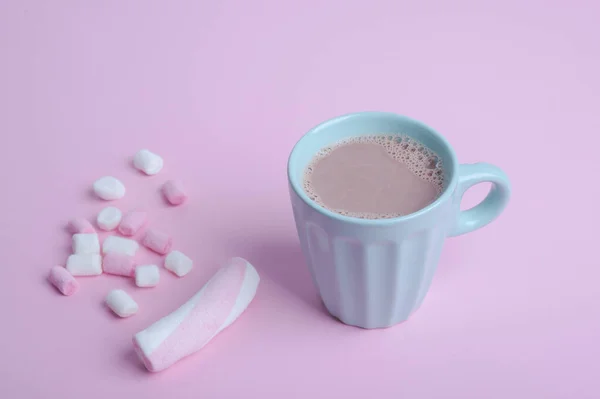 Mug warna biru dengan coklat dan marshmallow putih-merah muda pada latar belakang merah muda — Stok Foto