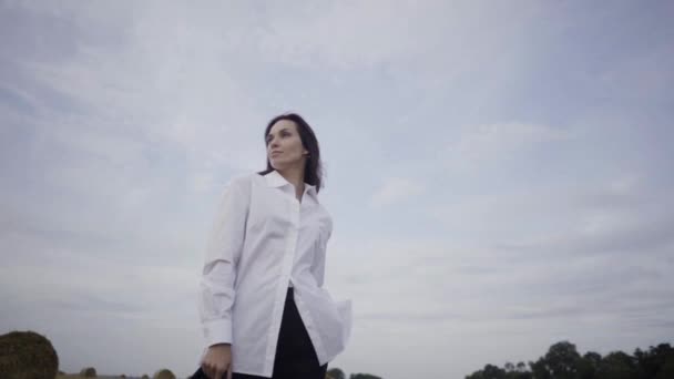 Красивая девушка в белой рубашке и черной куртке стоит в поле камера снимает вокруг девочек замедленной съемки — стоковое видео