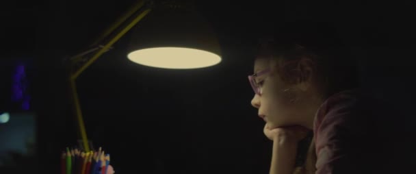 Malá školačka si nechce večer dělat domácí úkoly ve světle lampy. anamorfní snímek 2x — Stock video