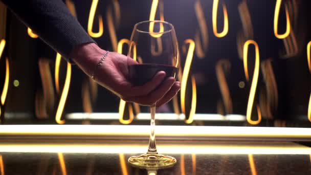 Szklanka czerwonego wina w męskiej dłoni potrząsa nim na ciemnym tle. zwolniony ruch — Wideo stockowe