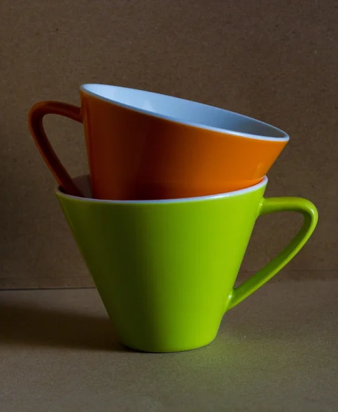 Tasse orange und grüne Tasse mit braunem Papphintergrund — Stockfoto