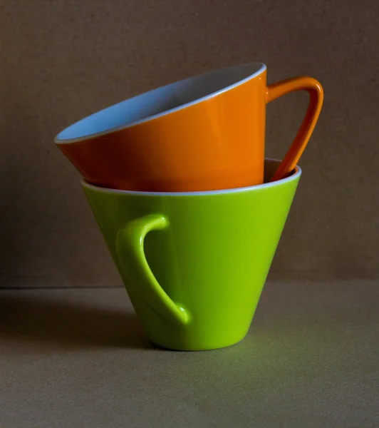 Чашка оранжевой и зеленой чашки с коричневым картонным фоном — стоковое фото