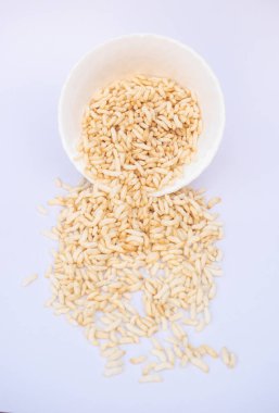 Beyaz kasedeki pirinçler hafif arka planda, kahvaltılık atıştırmalıklar ve aşçılık konseptine döküldü. Pofuduk pirinç, beyaz bir kaseden solgun bir yüzeye yuvarlanır..