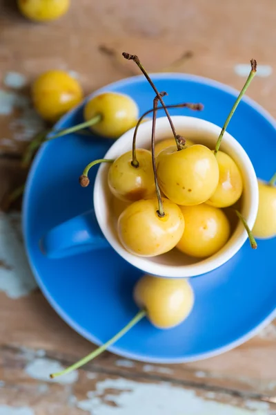 Blue tea cup full with yellow juicy cherries — Zdjęcie stockowe