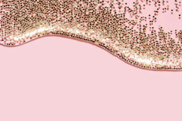 Şeffaf sıvı ve altın parıltısı pastel pembe arka plandan akıyor.