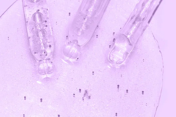 Zamknąć makro kroplomierza pipety płynem z cząstkami na fioletowym tle — Zdjęcie stockowe